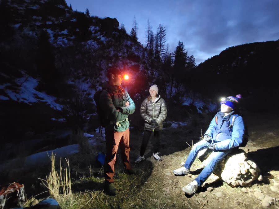 three people stand and talk near Fifth Water Hot Springs at night in Winter