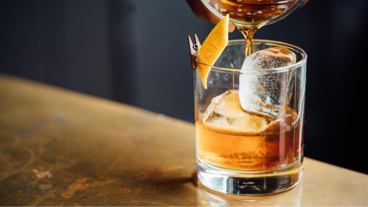 old fashioned being poured into whiskey tumbler