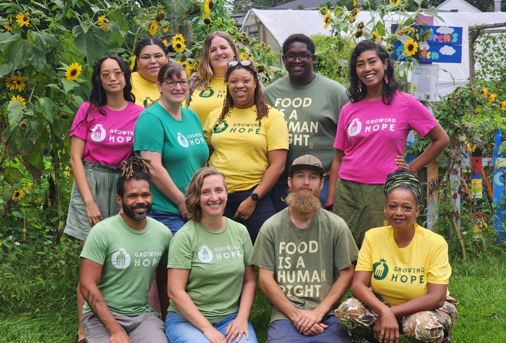Staff poses for photo outside surrounded by green grass and plants.