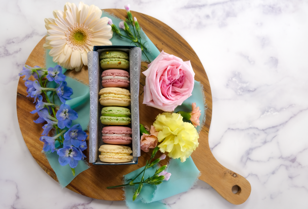 Six pack of colorful macarons on a serving board adorned in spring flowers.