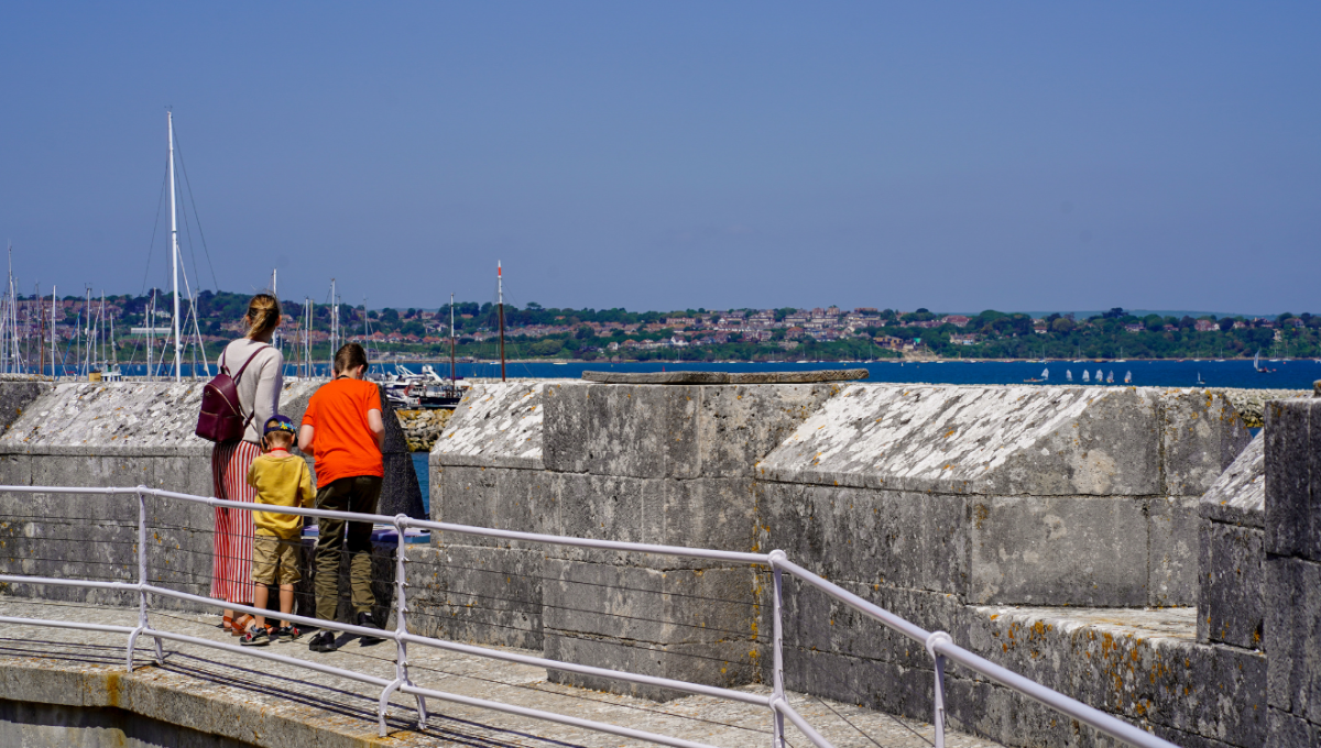 Family of three people looking out over the walls of Portland Castle towards Portland Harbour in Dorset