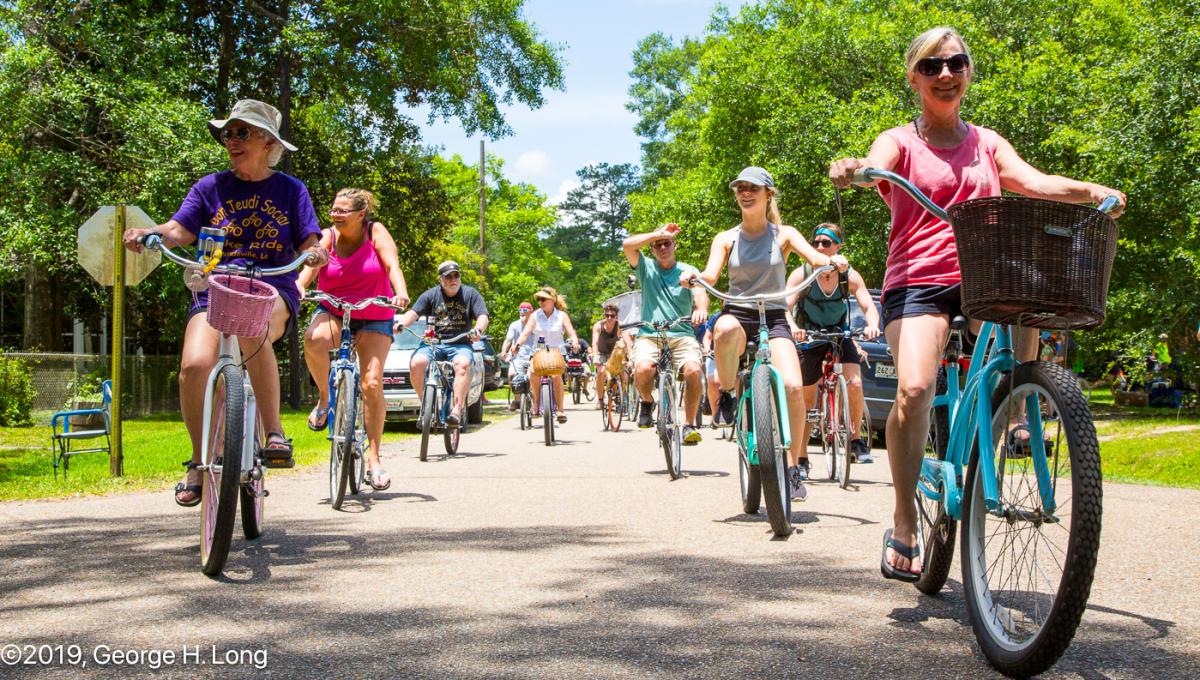 A group of cyclists rides together along a sunny, tree-lined Tammany Trace during the Louisiana Bicycle Festival.