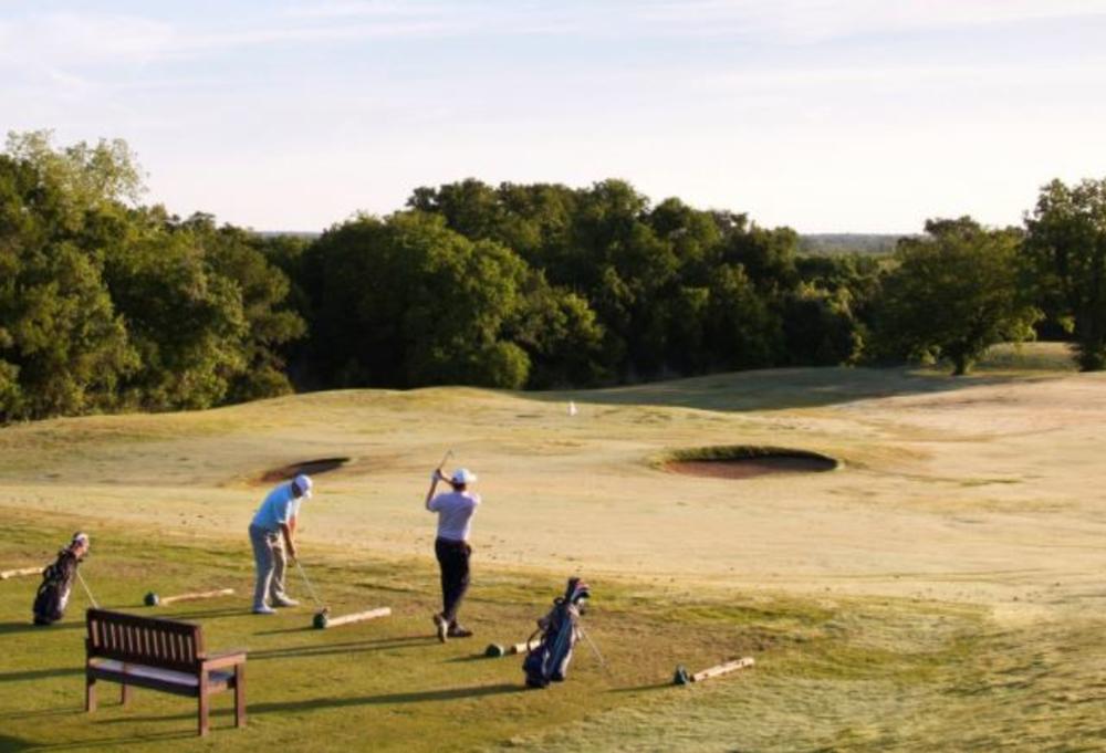 Two golfers swinging clubs with a vast golf course in front of them.