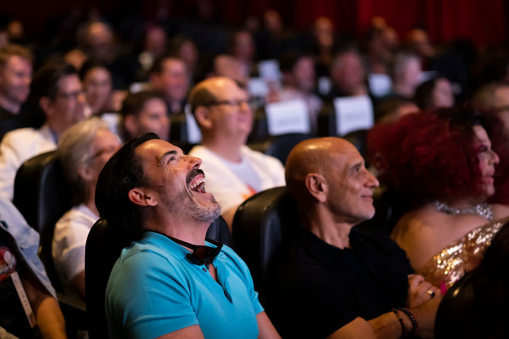 Close up of a man in a theater audience laughing with his head tilted back.