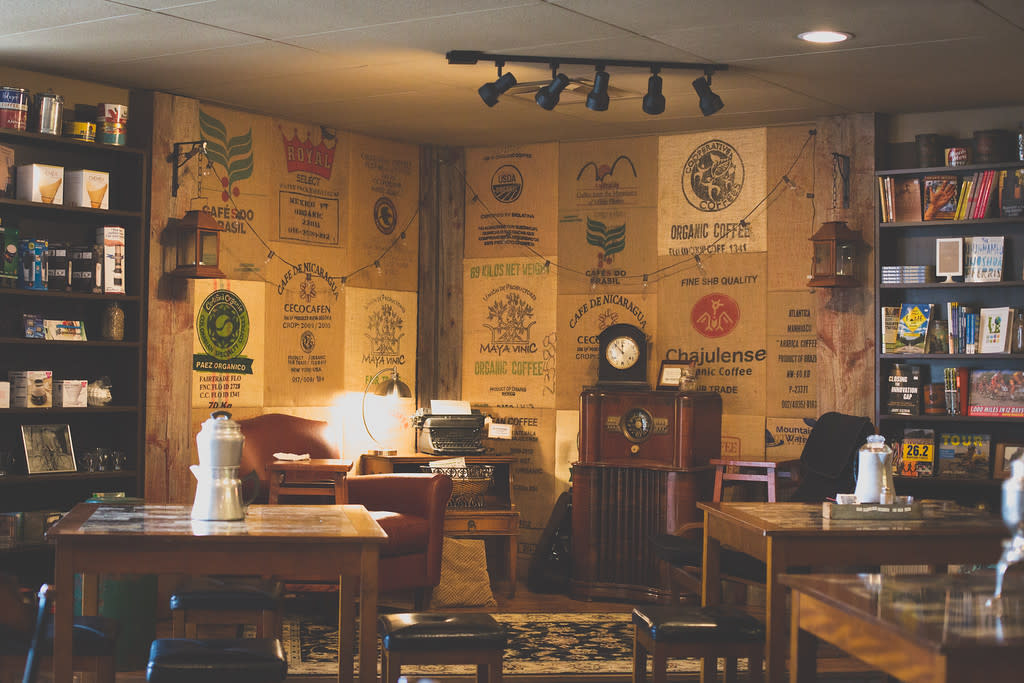 Image is of the inside of Velocity Bike & Bean where there is tables, chairs, book shelves with books and mugs.