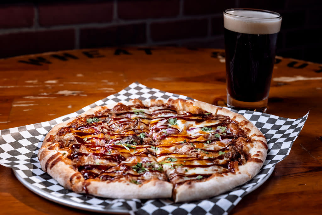 bbq chicken pizza on a platter in front of dark beer