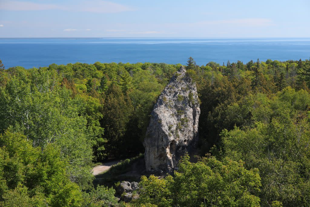 The limestone stack called Sugar Loaf towers above the green Mackinac Island forest with blue waters in the background
