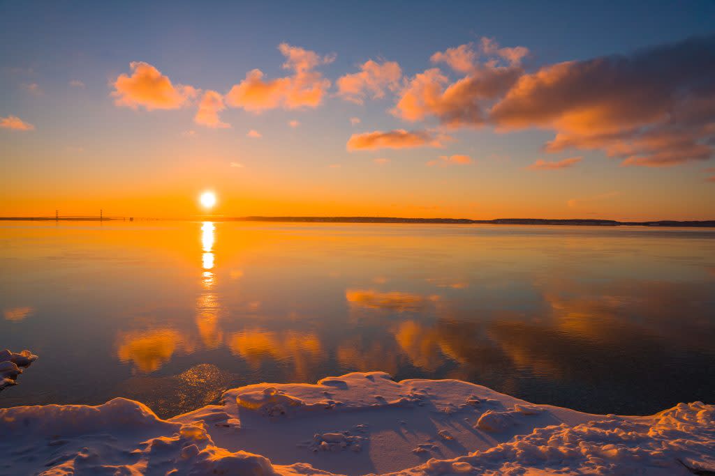 The sun sets beyond the Mackinac Bridge as seen from the snowy shore of Mackinac Island in winter