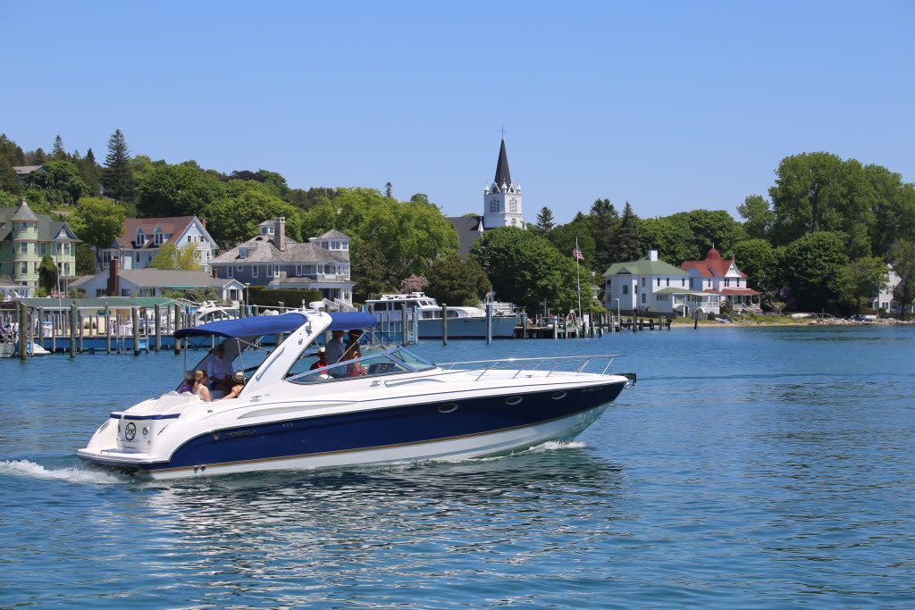 A boat cruises through the water off the coast of Michigan's Mackinac Island with Ste. Anne's Church in the background