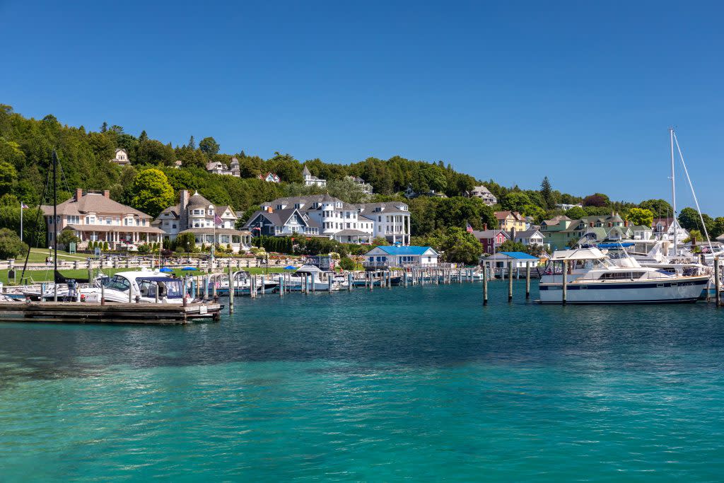 Boats sit docked in the crystal clear blue-green waters of the Mackinac Island harbor, with places to stay in the background
