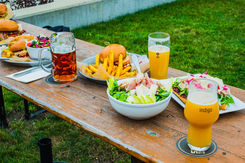 wooden table filled with burgers, fries, salads, and beer