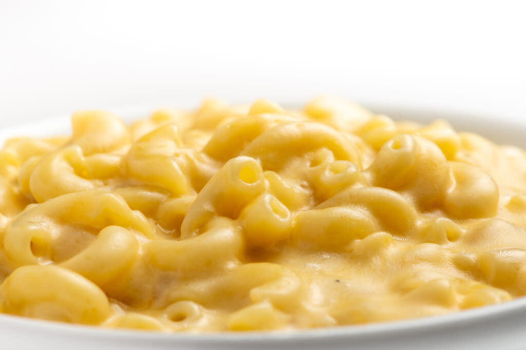 A close-up of creamy macaroni and cheese served on a white plate with a white background.