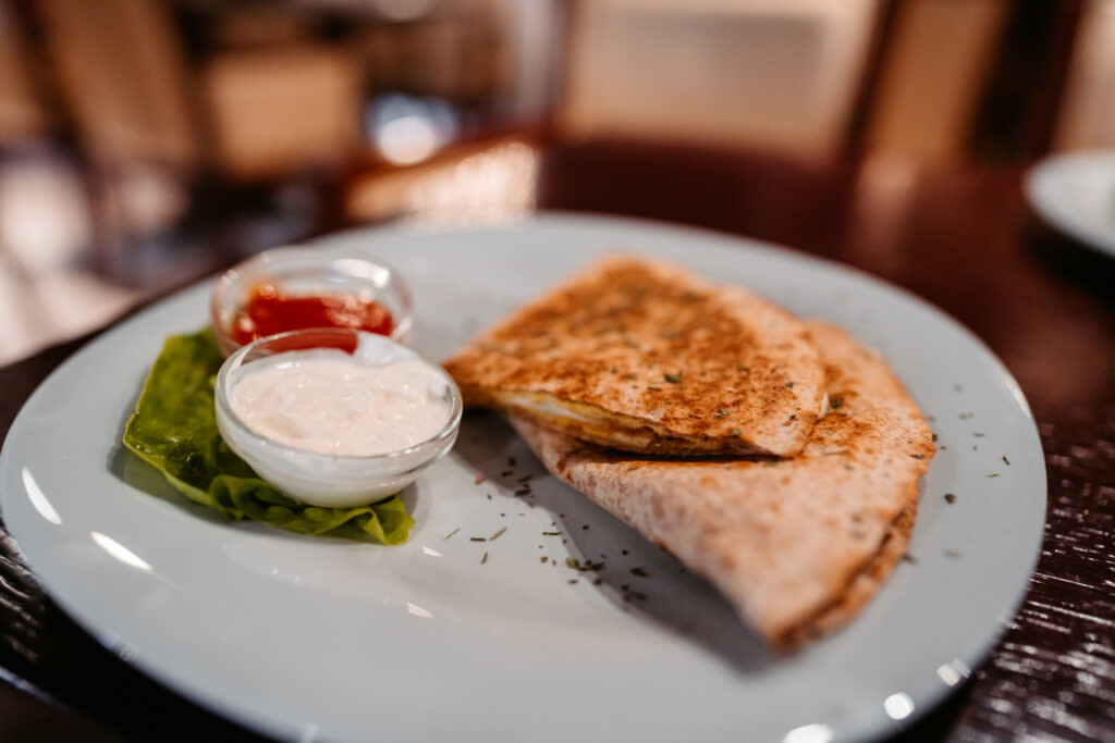 A grilled quesadilla served with sides of sour cream and ketchup on a blue plate.