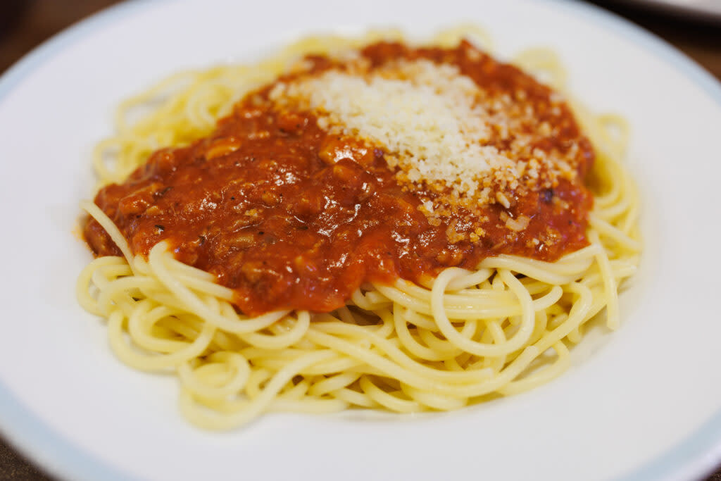 A plate of spaghetti topped with tomato sauce and sprinkled with grated cheese.