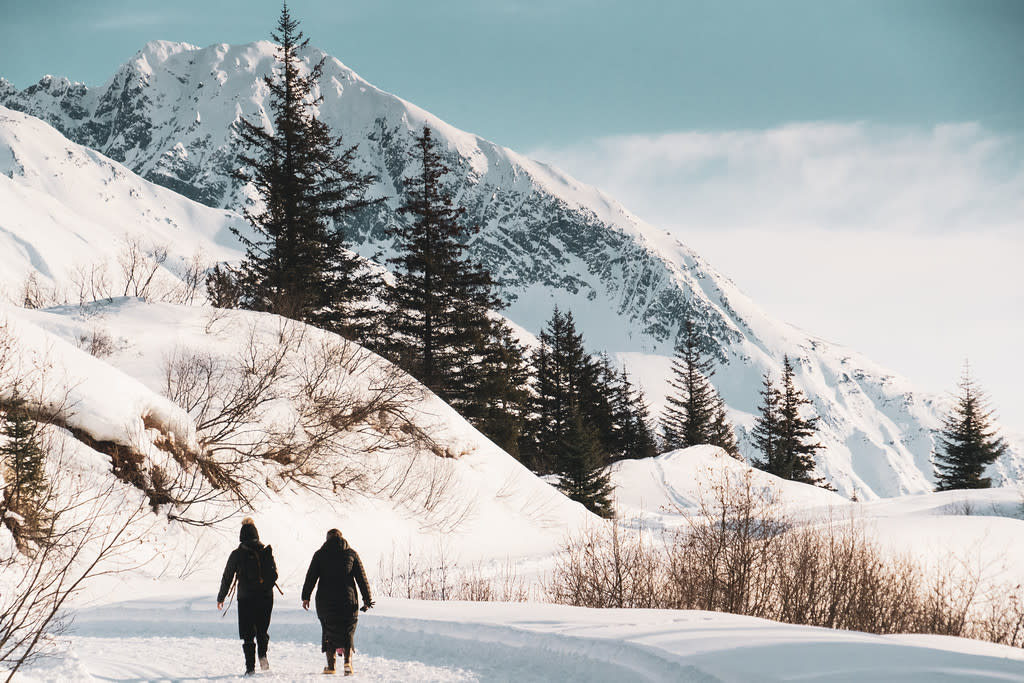 two people walking on a winter trail; mountains and evergreens in background