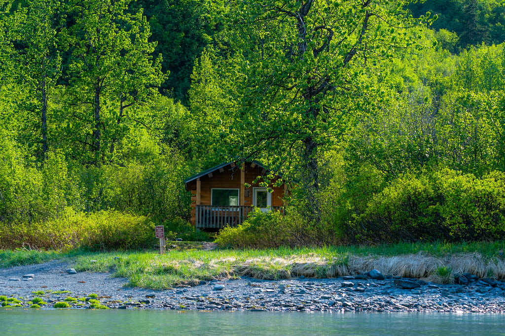 a cabin surrounded by trees on the shore of a bay