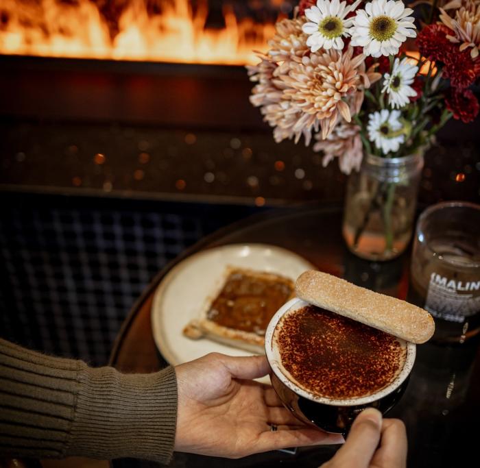Woman holds mug with latte with cookie resting on top of the full cup.