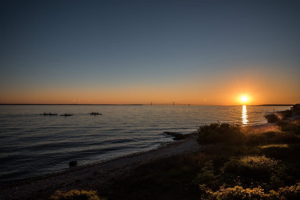 A fleet of kayaks paddle toward the sun as it sets beyond the Mackinac Bridge on a trip with Great Turtle Kayak Tours.