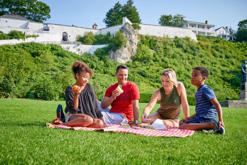 A family of four enjoys a picnic on the lawn of Mackinac Island’s Marquette Park in front of historic Fort Mackinac