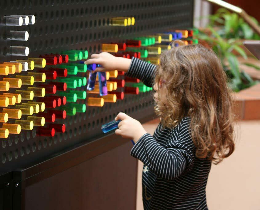 A girl plays with colorful pegs on an interactive exhibit as part of the Pixel Palace exhibit at Exploration Place