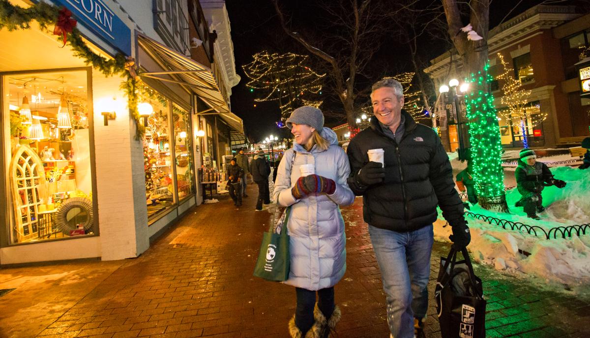 A couple of people bundled up with warm drinks walking along Pearl Street, enjoying their holiday shopping.