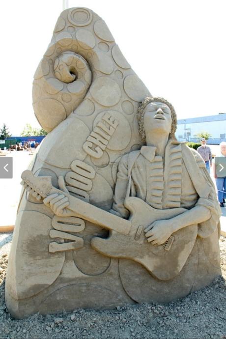 Sand sculpture of Jimi Hendrix rocking out on guitar. His background says Voodoo Chile and has a swirled backdrop.