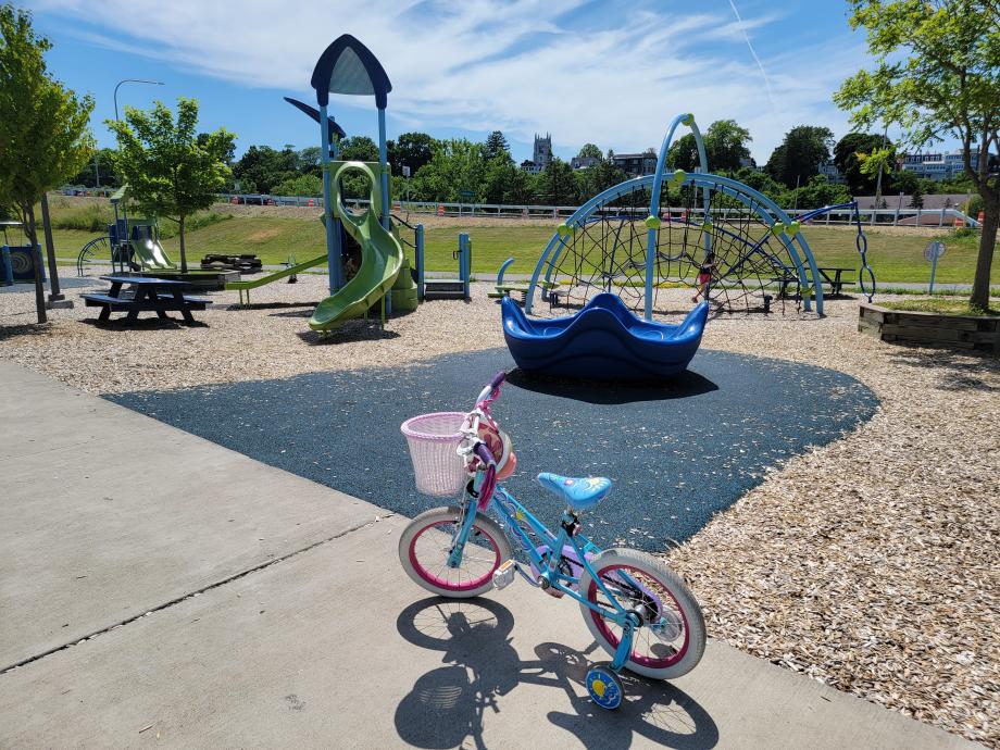pink and blue children's bike on sidewalk in front of play ground slide and spider web