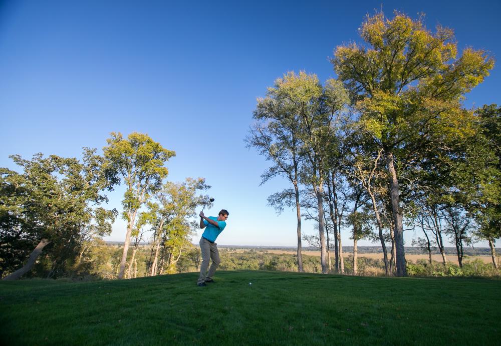 A golfer swinging a golf club to hit a golf ball in the grass