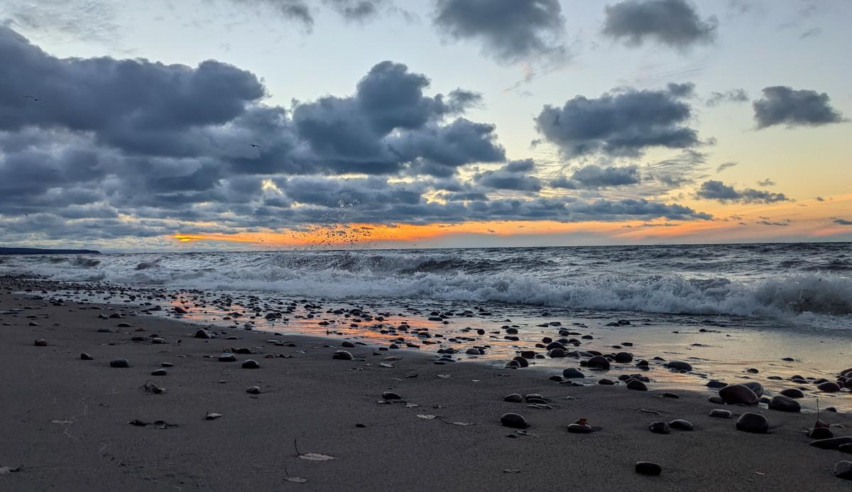 Sunset at Calumet Waterworks Beach. Many clouds, some rocks scattered on beach.