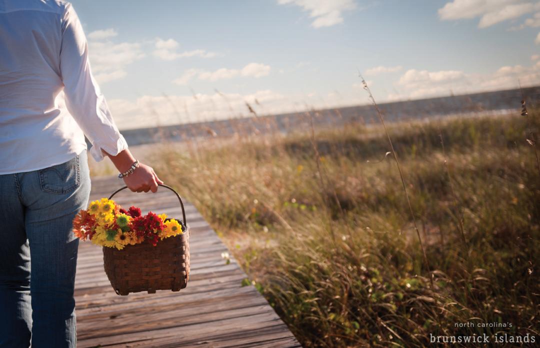 A visitor carries a picnic basket full of fresh cut flowers down a beach boardwalk.