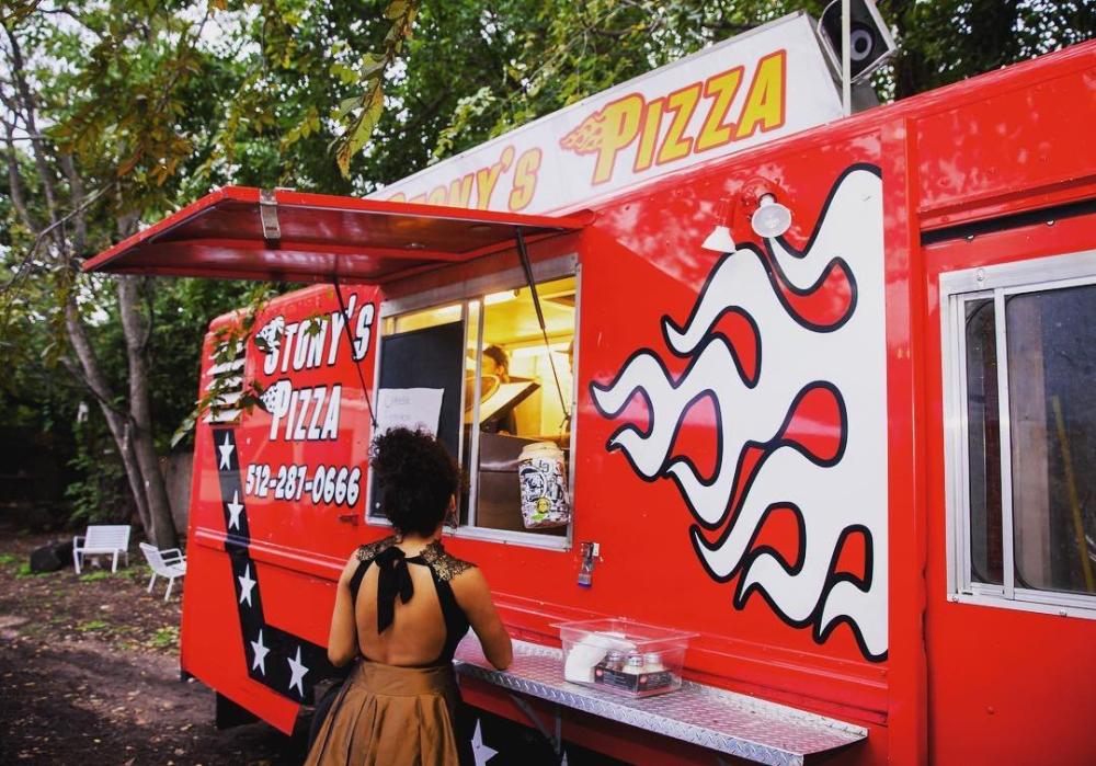 Woman standing at pickup window of food truck.