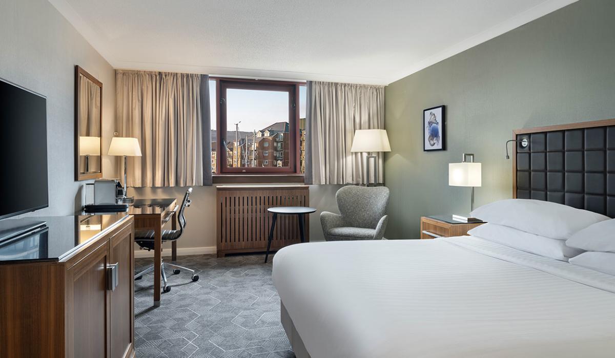 A contemporary hotel room with a bed, desk and TV.