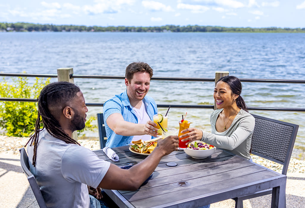 Two men and a woman sit at a table, enjoy lunch at the Cove Lakeside Bistro, while sitting in front of the lake.
