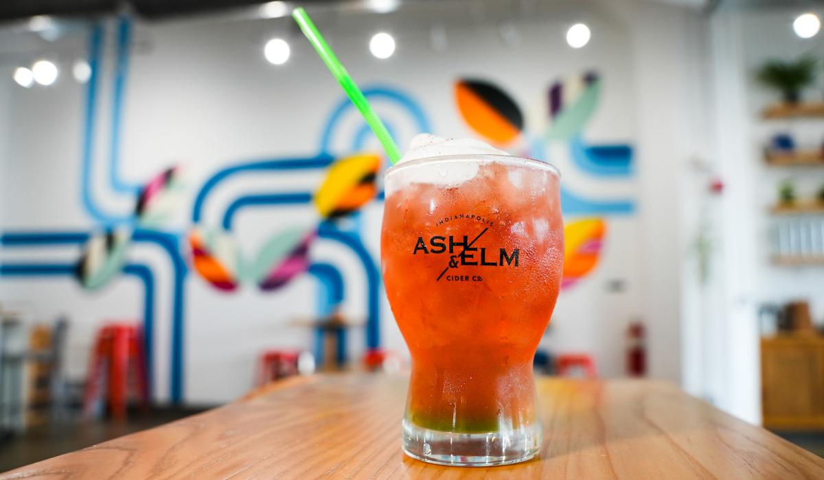 A wide glass with words "Ash & Elm" had red and orange drink