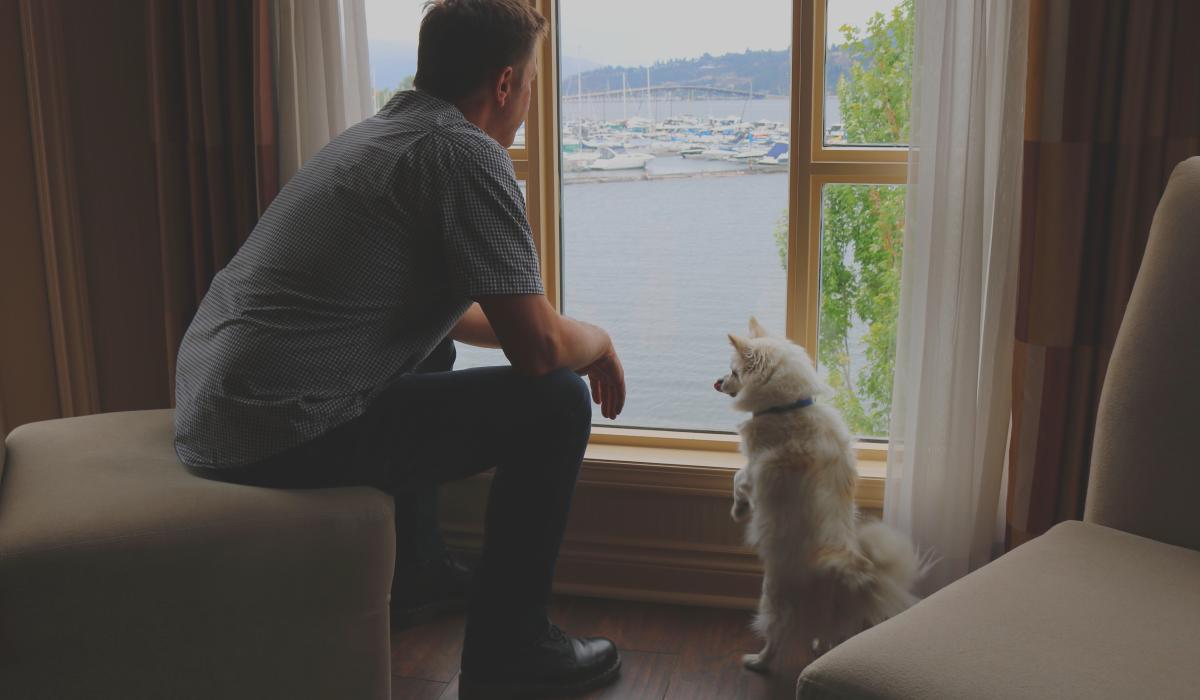 A man sits on a chair with his dog next to him on the floor as they look out the window of the Delta Hotel