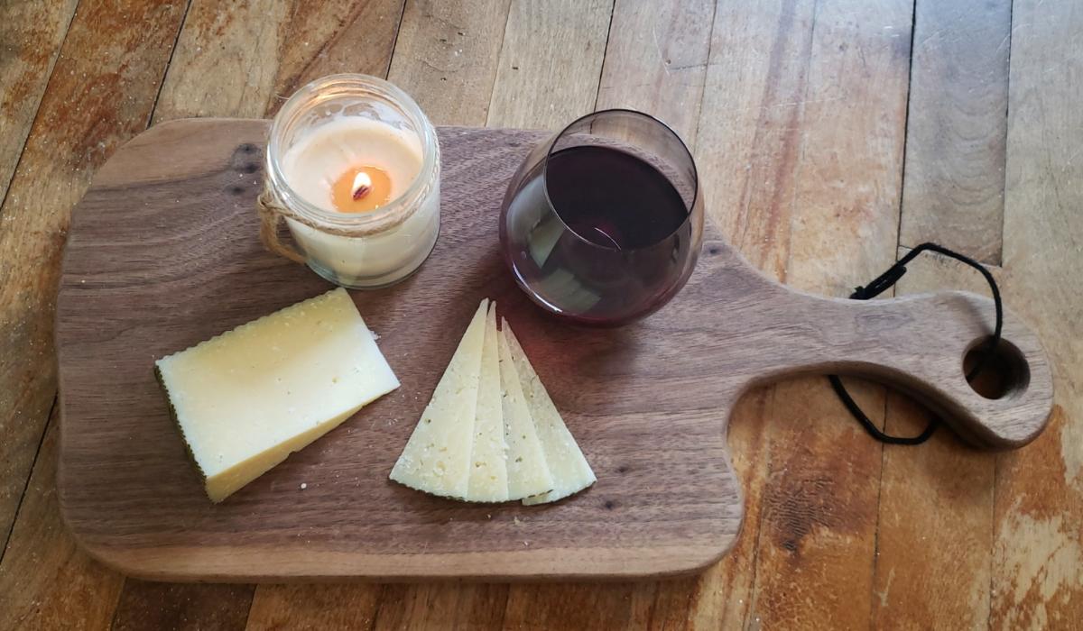 Cheese, wine, and a candle are seen on a wood cutting board.