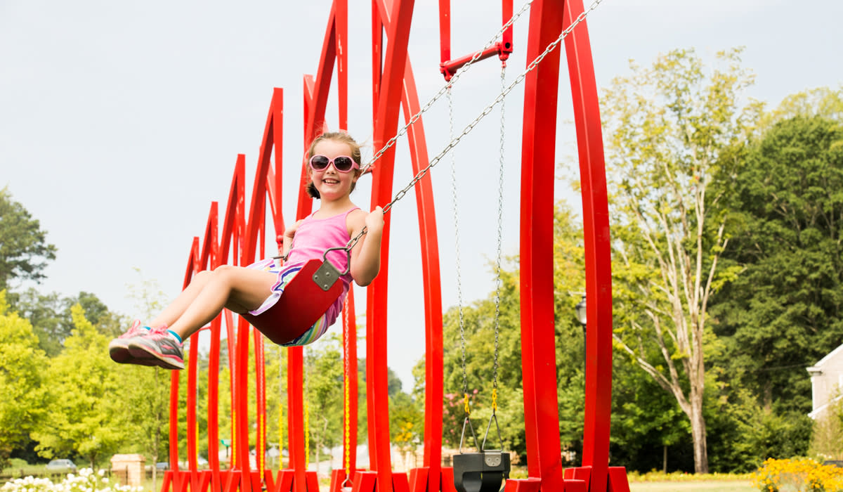 Charming little girl on the red swing set at Abernathy Greenway Playable Art Park