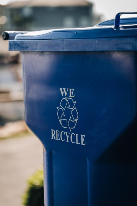 Close-up of a blue recycling bin outdoors with a white recycling symbol and the words “We Recycle” printed on the side.