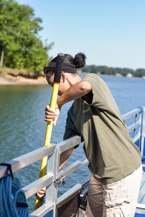 A woman using a pole to collect a water sample from Lake Norman while on the Catawba Riverkeeper Floating Classroom.