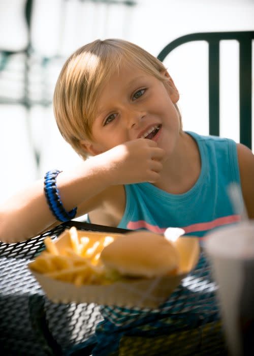 A young blond boy is eating fries and a hamburger at Gilroy Gardens