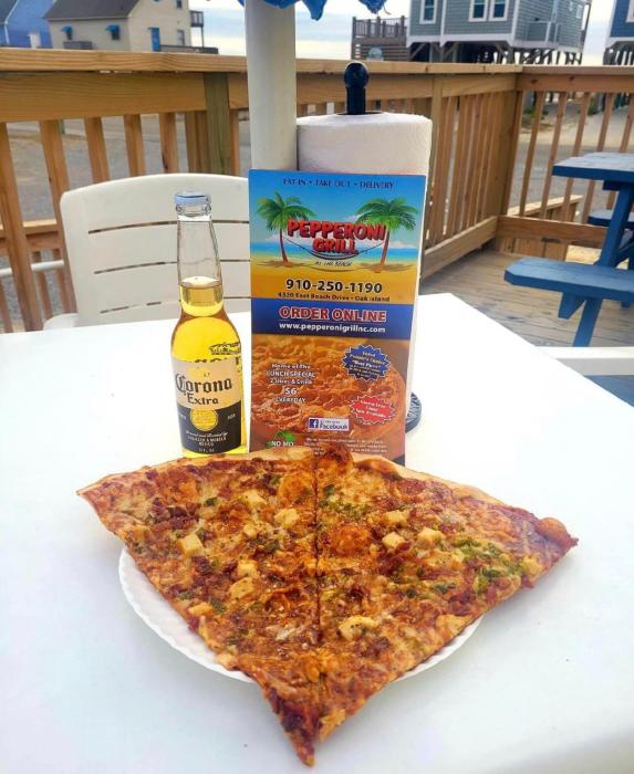 a plate with two large slices of pizza and a beer on an outside patio near the beach
