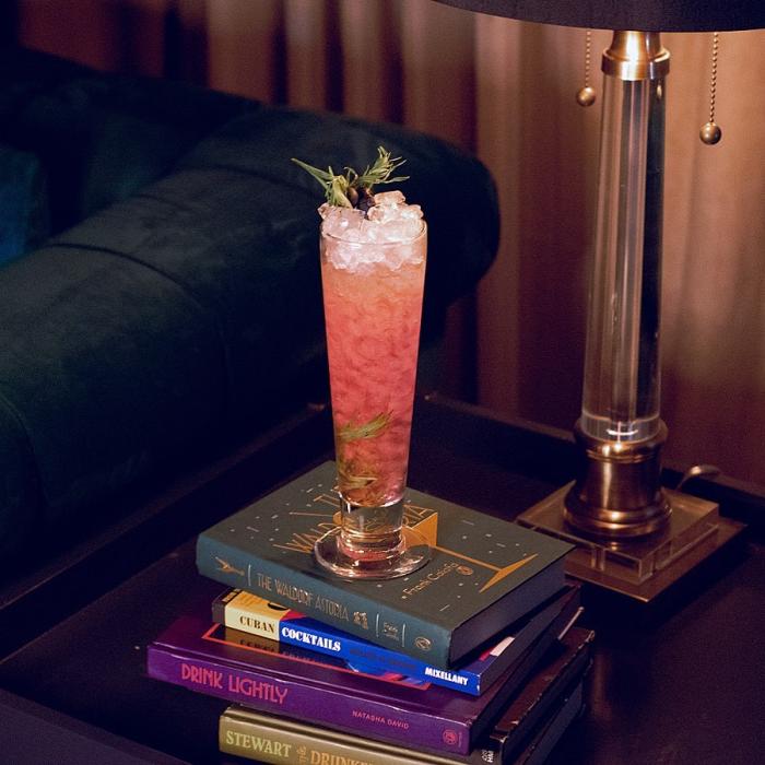 a Blueberry Hill cocktail sits on a stack of cocktail books at The Copper Lounge