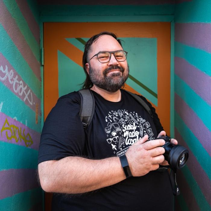 A man with a camera in front of a colourful entry way.