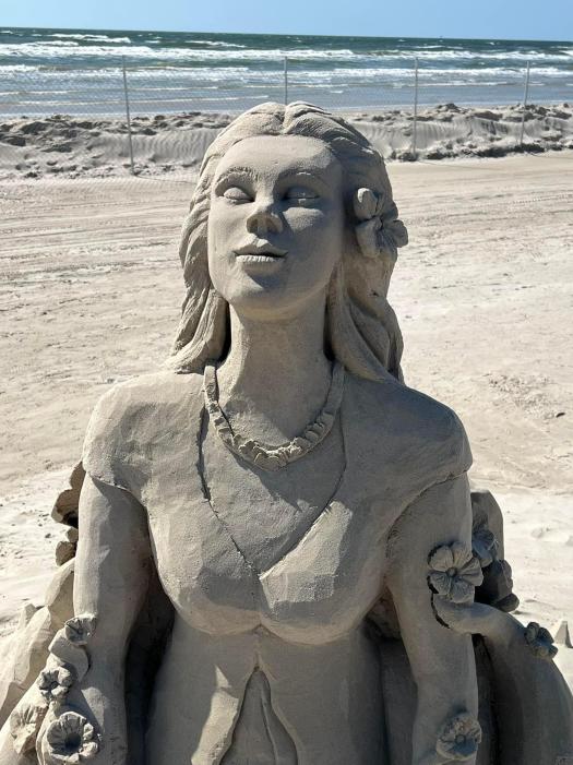 Close up of a sand sculptor that shows a woman looking up to the sky. Her arms are down and covered in vines and flowers