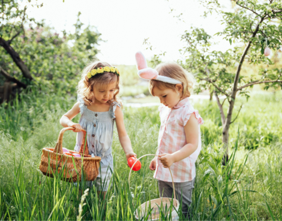 Two little girls wearing Easter headdresses collect eggs in baskets in the garden