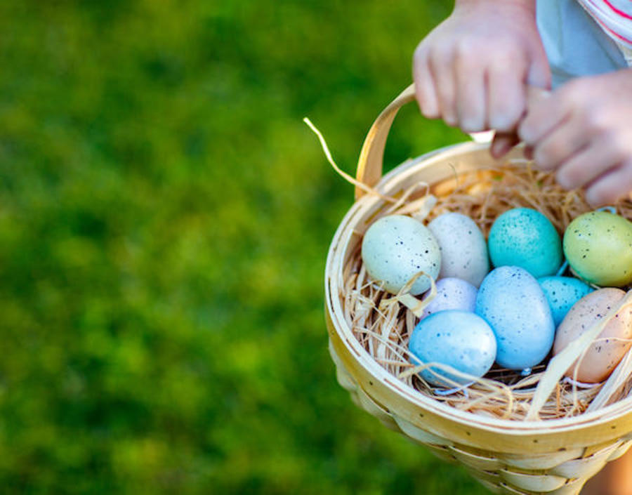 A child holds a basket of coloured eggs