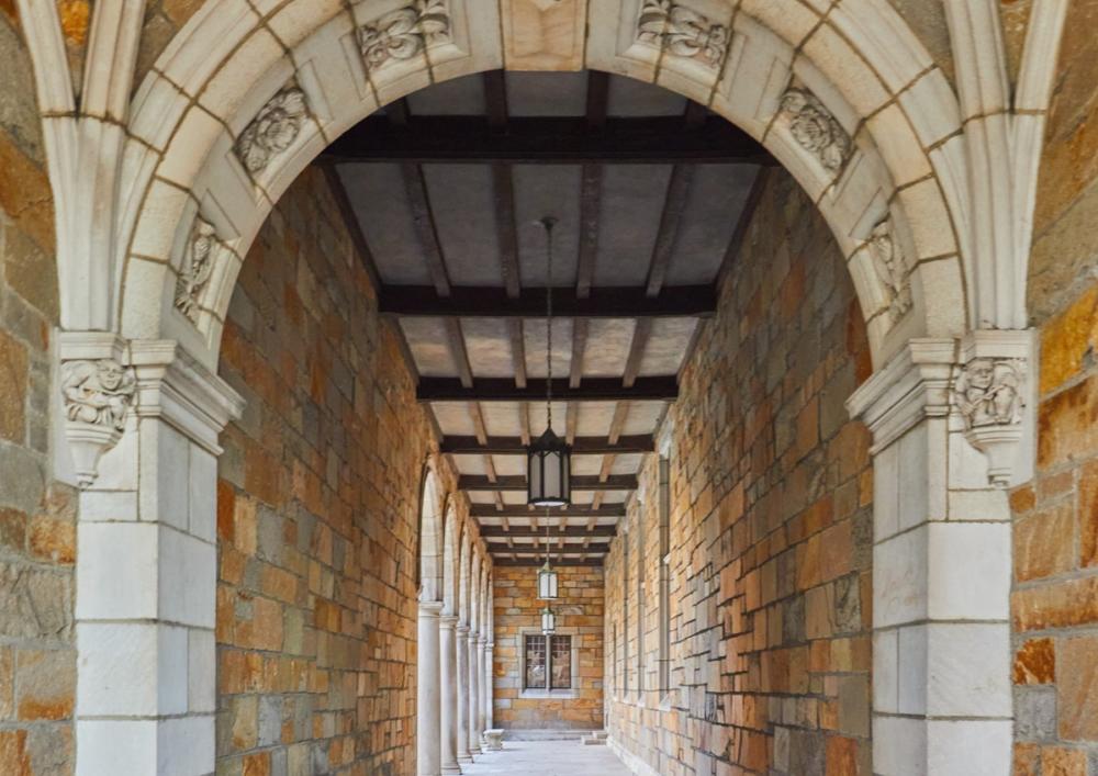 View of long outdoor pathway covered by building stones and intricate structures supporting the building's exterior.