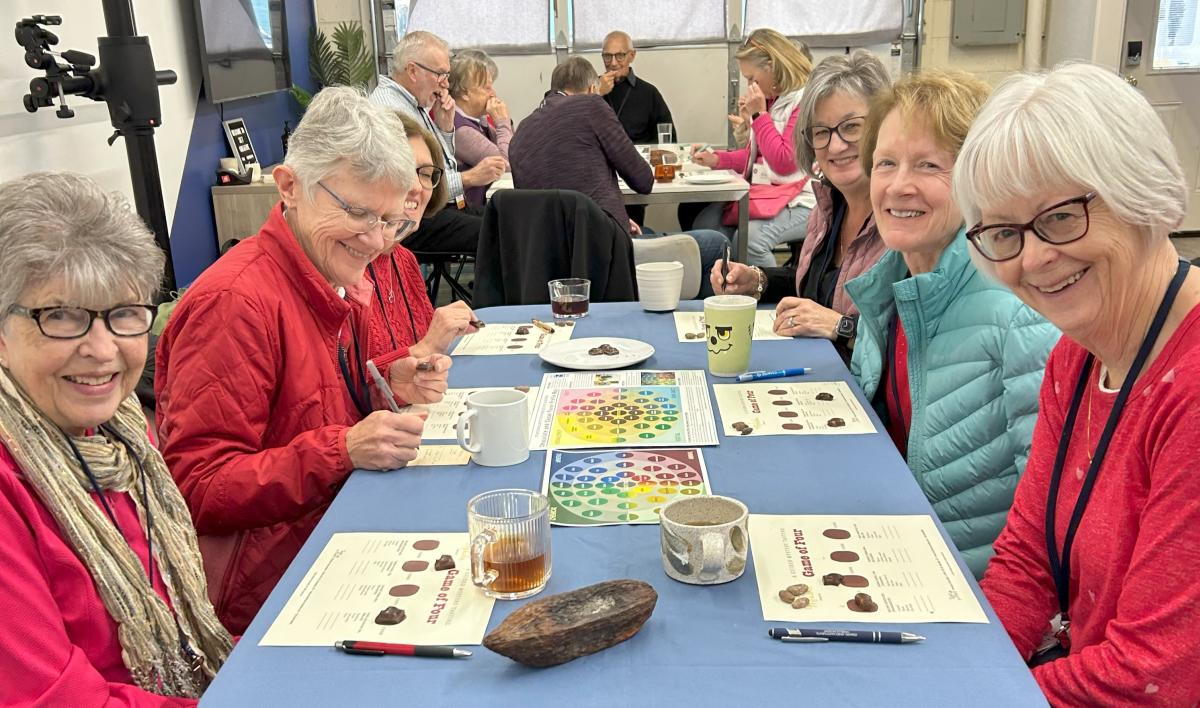 Six women sit at a table with choclates before them for a Moksha Chocolate Workshop