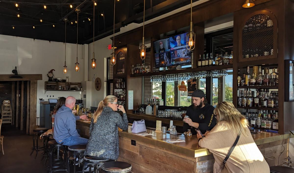 Image is of Boomtown's bar with people sitting around it and the bartender pouring drinks.