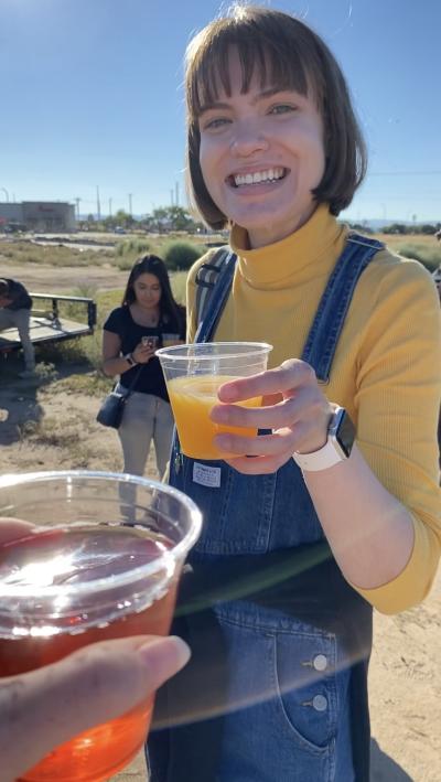 A young woman wearing a yellow turtleneck and overalls holds a mimosa
